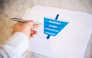 Male hand pointing at a printed AARRR Marketing sales funnel - Acquisition Activation Retention Revenue Referral, coffee, props,